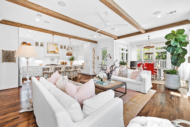 living room featuring ceiling fan with notable chandelier, beamed ceiling, and dark hardwood / wood-style flooring