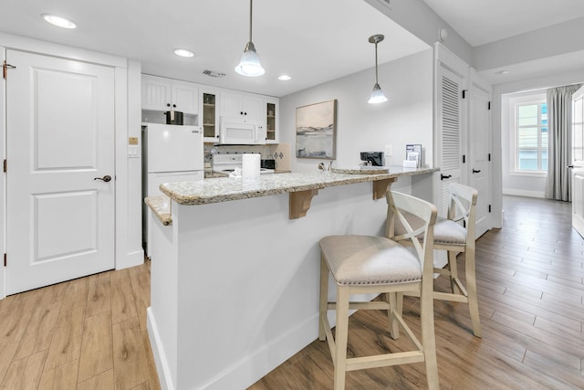 kitchen with white appliances, decorative light fixtures, light stone counters, white cabinets, and light hardwood / wood-style floors