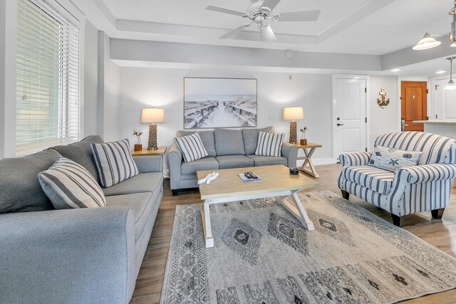 living room featuring a raised ceiling, ceiling fan, and light hardwood / wood-style floors