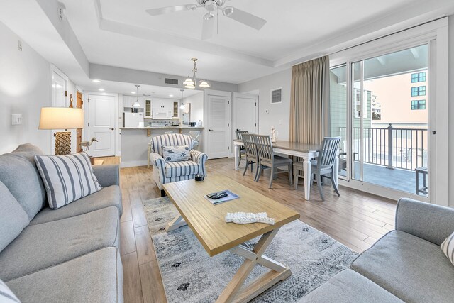 living room with a tray ceiling, ceiling fan with notable chandelier, and light hardwood / wood-style floors