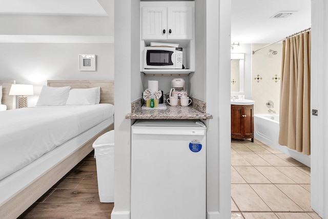 bedroom with light tile patterned floors, ensuite bath, visible vents, and a sink