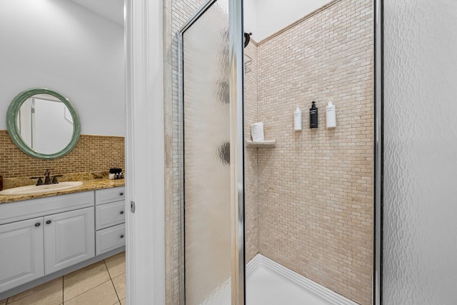 bathroom featuring vanity, a shower with shower door, decorative backsplash, and tile patterned flooring