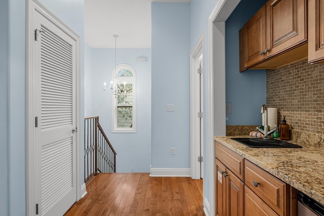 kitchen featuring an inviting chandelier, light hardwood / wood-style flooring, decorative light fixtures, light stone counters, and sink