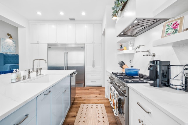 kitchen with sink, light stone counters, light wood-type flooring, white cabinets, and premium appliances