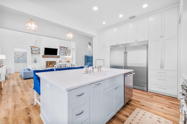 kitchen featuring light wood-type flooring, a kitchen island with sink, white cabinets, appliances with stainless steel finishes, and sink