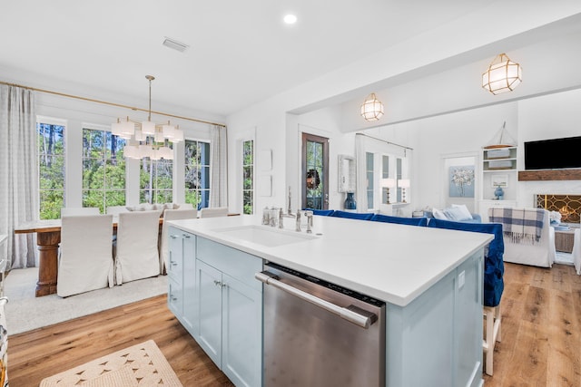 kitchen featuring sink, light wood-type flooring, a kitchen island with sink, dishwasher, and hanging light fixtures