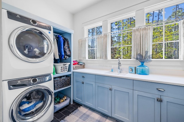 washroom with stacked washer / drying machine, sink, cabinets, and dark tile patterned floors