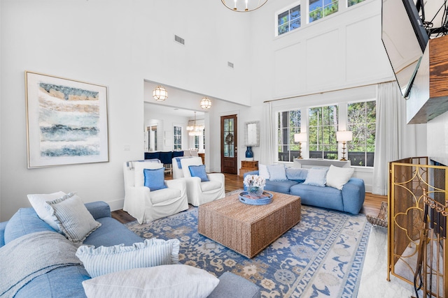 living room with an inviting chandelier, hardwood / wood-style flooring, and a towering ceiling