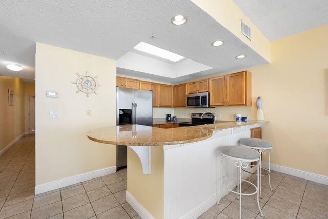 kitchen featuring a kitchen breakfast bar, light tile patterned floors, stainless steel appliances, and kitchen peninsula