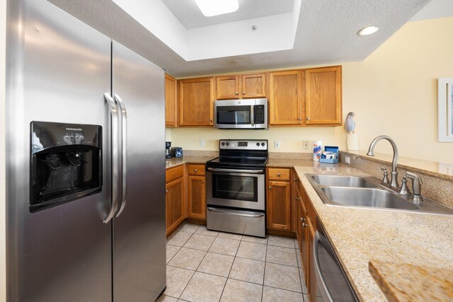 kitchen with a textured ceiling, light tile patterned floors, appliances with stainless steel finishes, sink, and light stone counters