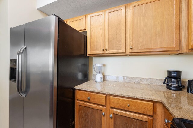 kitchen featuring a textured ceiling, black range, light stone counters, and stainless steel refrigerator with ice dispenser