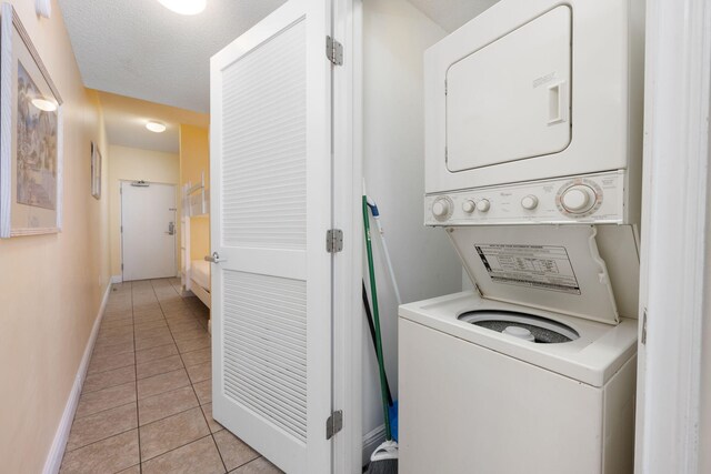 clothes washing area with light tile patterned floors, stacked washing maching and dryer, and a textured ceiling