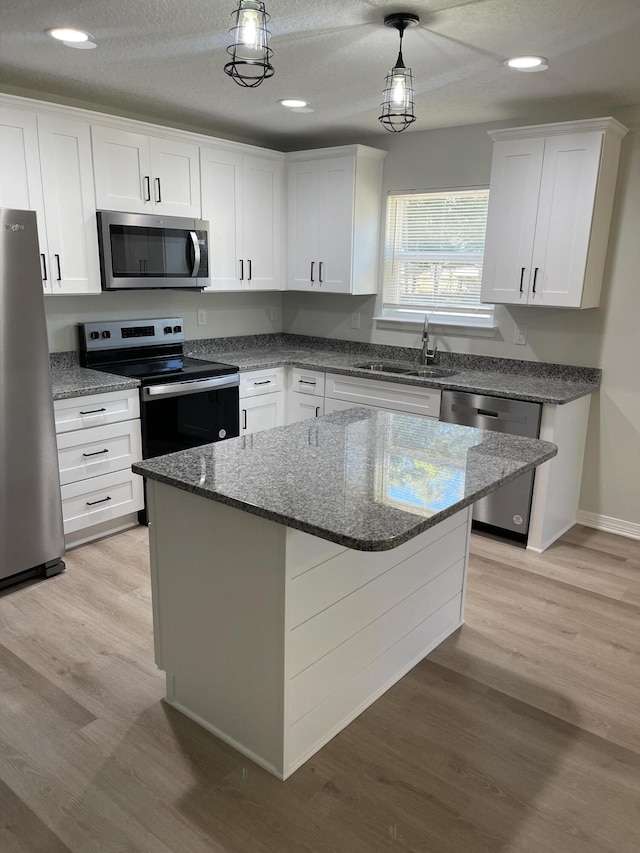 kitchen featuring a center island, sink, appliances with stainless steel finishes, decorative light fixtures, and white cabinetry