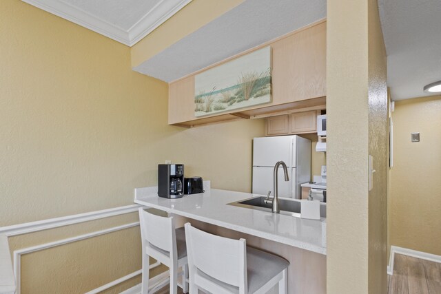 kitchen featuring sink, crown molding, a kitchen bar, light brown cabinetry, and white appliances