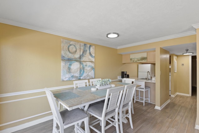 dining area with crown molding, light wood-style flooring, and baseboards