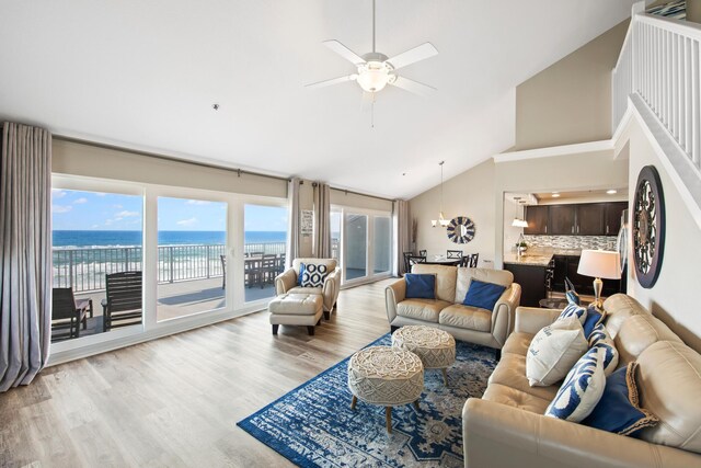 living room with ceiling fan with notable chandelier, high vaulted ceiling, a water view, and light wood-type flooring