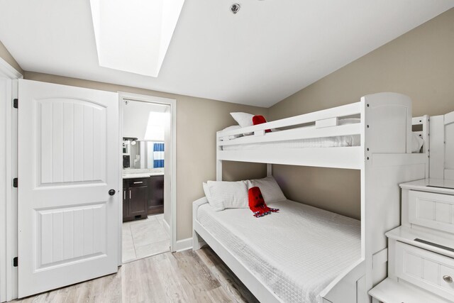 bedroom featuring light hardwood / wood-style floors, connected bathroom, and lofted ceiling with skylight