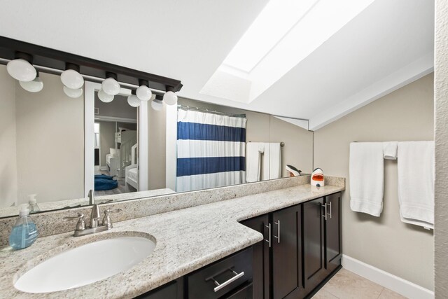 bathroom with vaulted ceiling with skylight, tile patterned flooring, and vanity