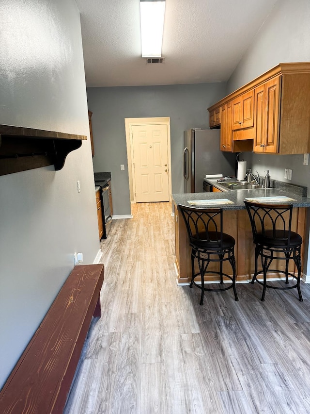 kitchen with hardwood / wood-style floors, sink, kitchen peninsula, stainless steel fridge, and a breakfast bar