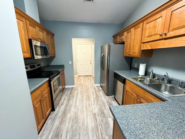 kitchen with appliances with stainless steel finishes, light hardwood / wood-style floors, vaulted ceiling, and sink