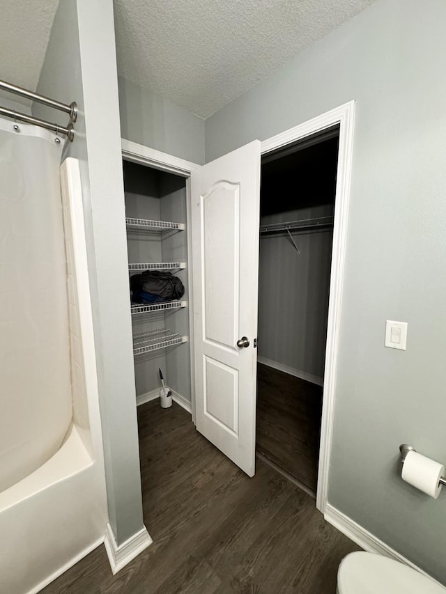 interior space featuring a textured ceiling, toilet, tub / shower combination, and wood-type flooring