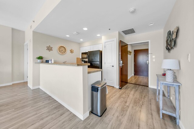 kitchen featuring light hardwood / wood-style floors, kitchen peninsula, white cabinetry, and black appliances