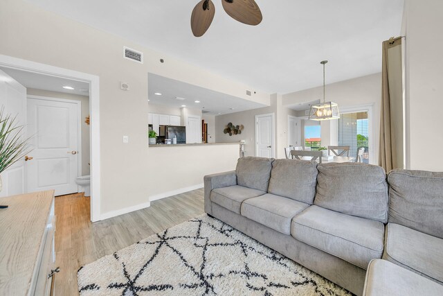 living room with light hardwood / wood-style floors and ceiling fan with notable chandelier