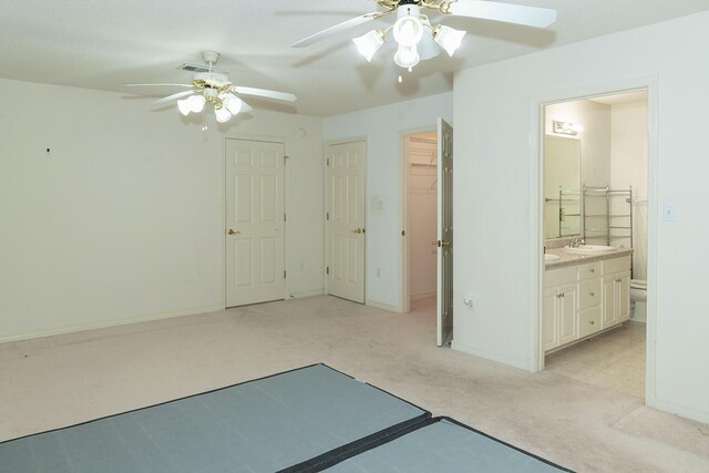 unfurnished bedroom featuring light carpet, sink, ceiling fan, a closet, and ensuite bathroom