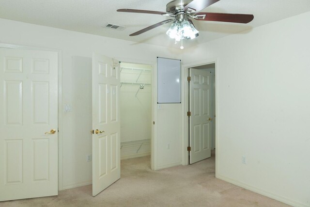 unfurnished bedroom with a closet, ceiling fan, a spacious closet, and light carpet