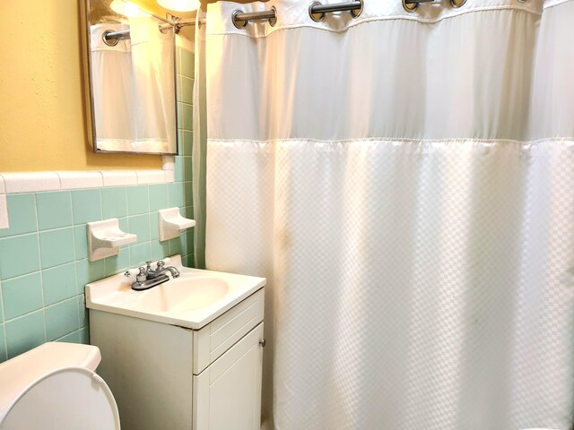 bathroom featuring a shower with shower curtain, toilet, tile walls, decorative backsplash, and vanity