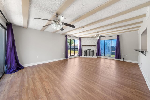 unfurnished living room with ceiling fan, light wood-type flooring, a textured ceiling, and a stone fireplace