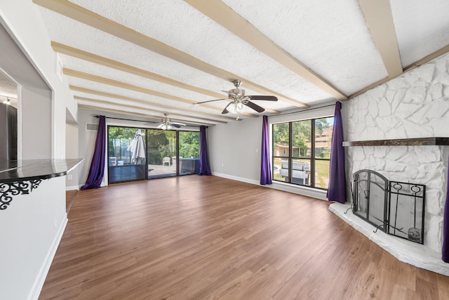 unfurnished living room featuring ceiling fan, hardwood / wood-style floors, a fireplace, a textured ceiling, and beamed ceiling