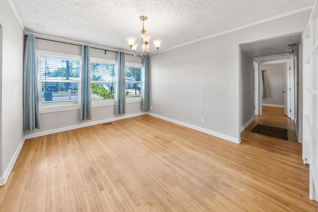 spare room with light wood-type flooring, ornamental molding, a textured ceiling, and a chandelier