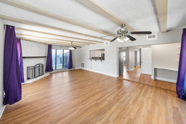 unfurnished living room with sink, beamed ceiling, a textured ceiling, ceiling fan, and hardwood / wood-style flooring