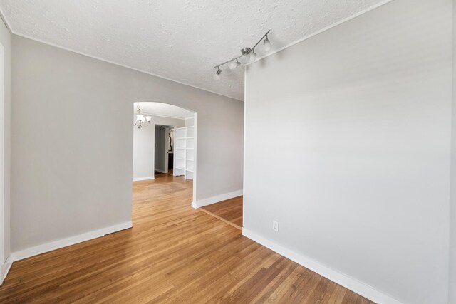 unfurnished room with rail lighting, a textured ceiling, and hardwood / wood-style floors