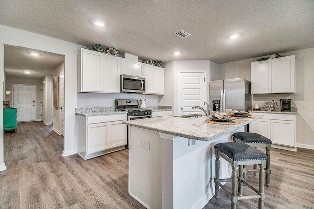 kitchen featuring light wood-type flooring, an island with sink, stainless steel appliances, and white cabinets