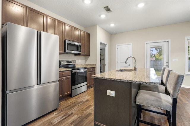 kitchen featuring appliances with stainless steel finishes, a kitchen breakfast bar, dark hardwood / wood-style floors, a kitchen island with sink, and sink