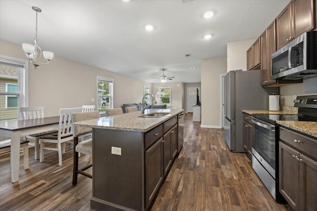 kitchen featuring sink, a center island with sink, appliances with stainless steel finishes, dark hardwood / wood-style floors, and ceiling fan with notable chandelier