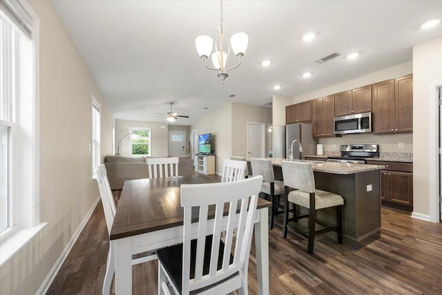 dining space with sink, ceiling fan with notable chandelier, and dark hardwood / wood-style flooring