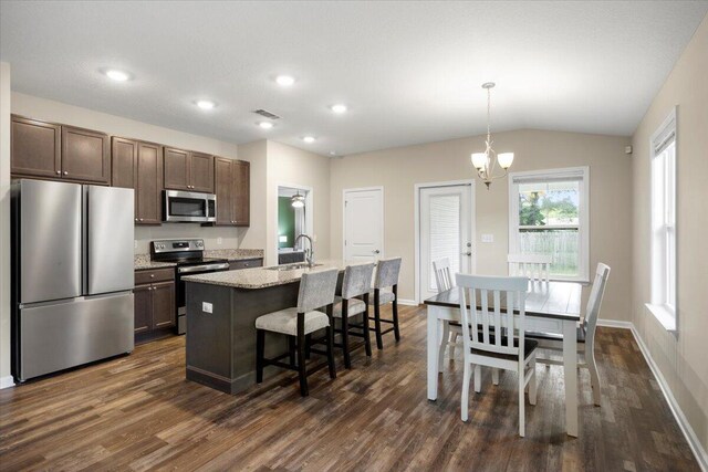 kitchen featuring pendant lighting, dark brown cabinets, a kitchen island with sink, stainless steel appliances, and vaulted ceiling