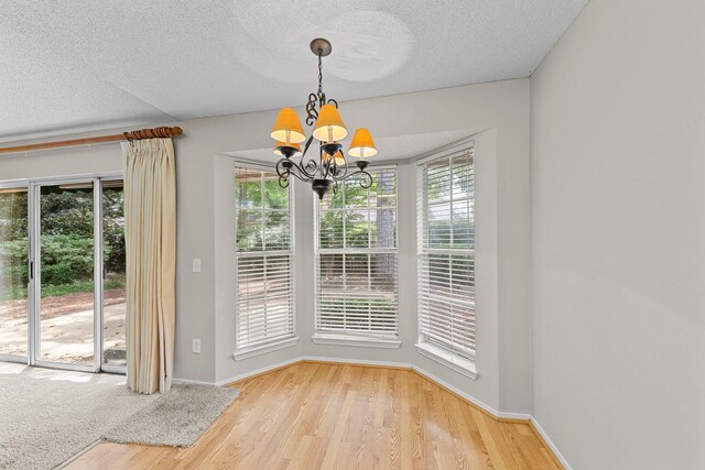 unfurnished dining area featuring light hardwood / wood-style floors, a notable chandelier, and a textured ceiling