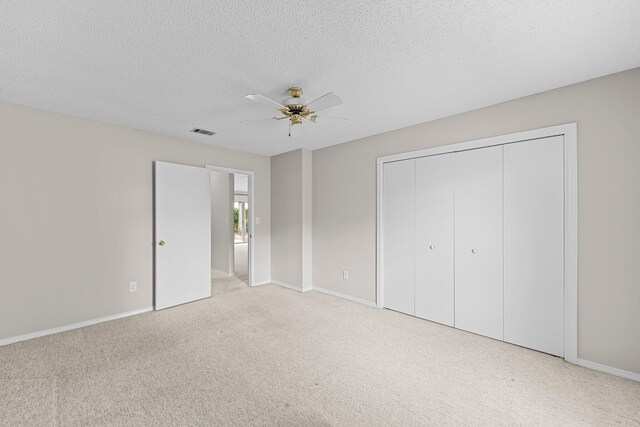 unfurnished bedroom with a textured ceiling, a closet, ceiling fan, and light carpet