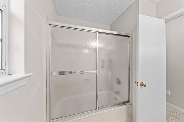 bathroom featuring a textured ceiling and a shower with shower door