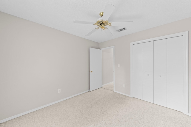 unfurnished bedroom with a textured ceiling, light colored carpet, ceiling fan, and a closet