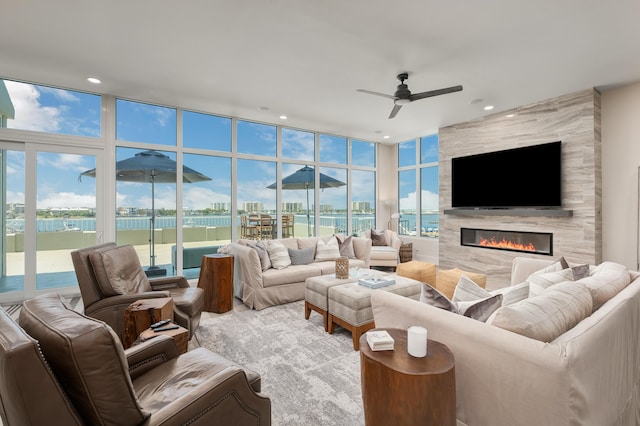 living room with a tiled fireplace, tile walls, ceiling fan, and a wall of windows