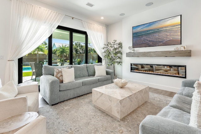 living area featuring recessed lighting, visible vents, a glass covered fireplace, wood finished floors, and baseboards