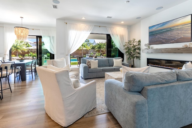 living area with wood finished floors, a glass covered fireplace, visible vents, and recessed lighting