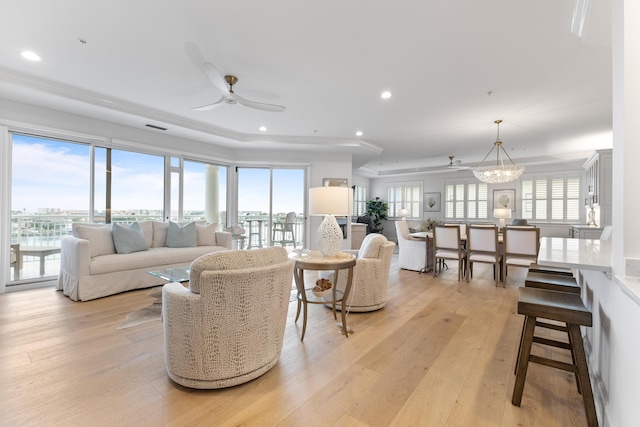 living area featuring visible vents, plenty of natural light, ceiling fan with notable chandelier, and light wood-type flooring