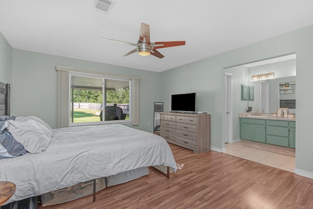 bedroom with light wood-type flooring, ceiling fan, connected bathroom, and sink