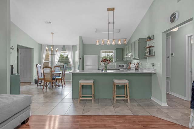 kitchen featuring green cabinets, decorative light fixtures, light wood-type flooring, white appliances, and kitchen peninsula